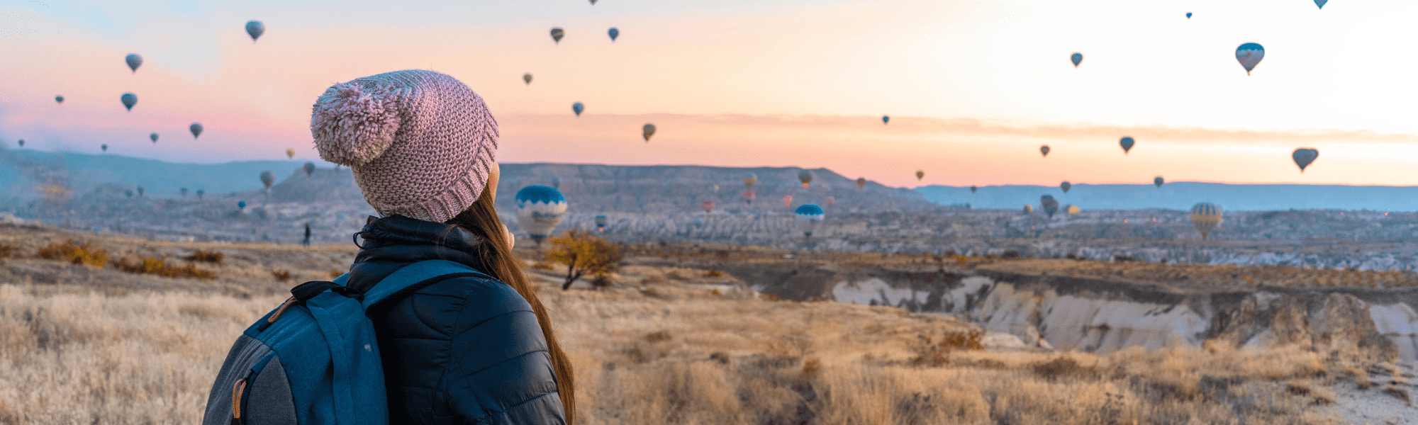 woman in a field observing hot air balloons 
