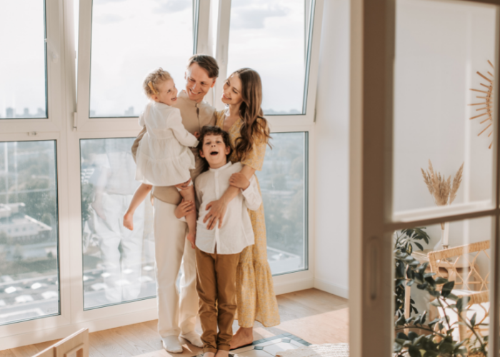 smiling family standing together in front of floor to ceiling windows 